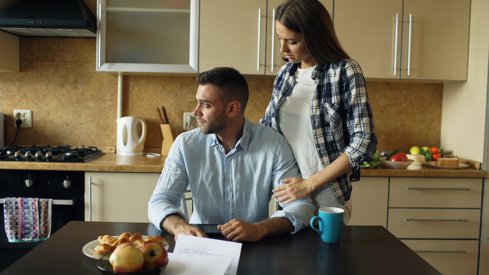 A man going through unpaid bills at the kitchen table, his partner beside him
